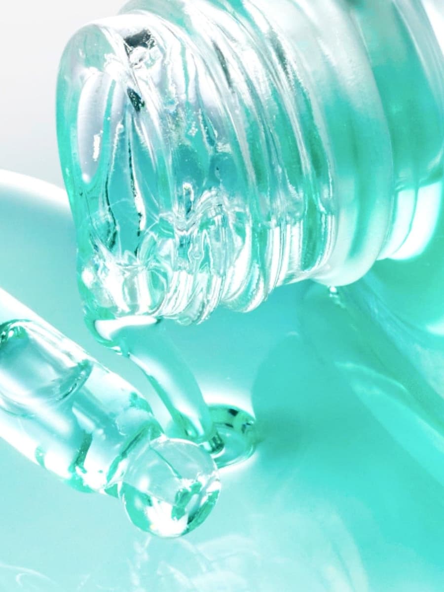 Official close-up of Anua's clear dropper and emerald serum capsules in a watery turquoise texture