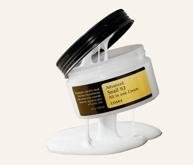 COSRX Advanced Snail 92 cream jar with a glossy white gel-cream ribbon on a warm ivory background