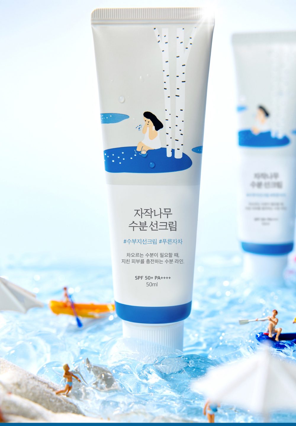 ROUND LAB Birch Juice Moisturizing Sunscreen tube standing on ice and water with miniature beach figures around it